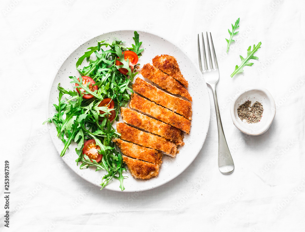 Traditional chicken schnitzel with arugula cherry tomatoes salad on light background, top view