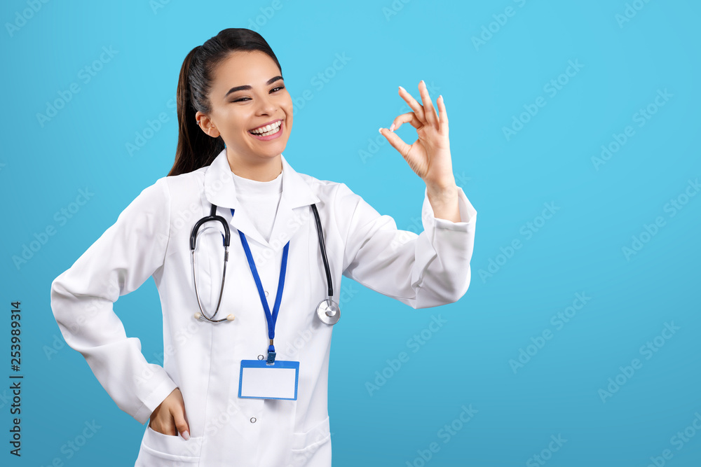 Portrait of pretty young woman doctor with stethoscope show ok gesture over blue background. Portrait of pretty young woman doctor with stethoscope show ok gesture over blue background.