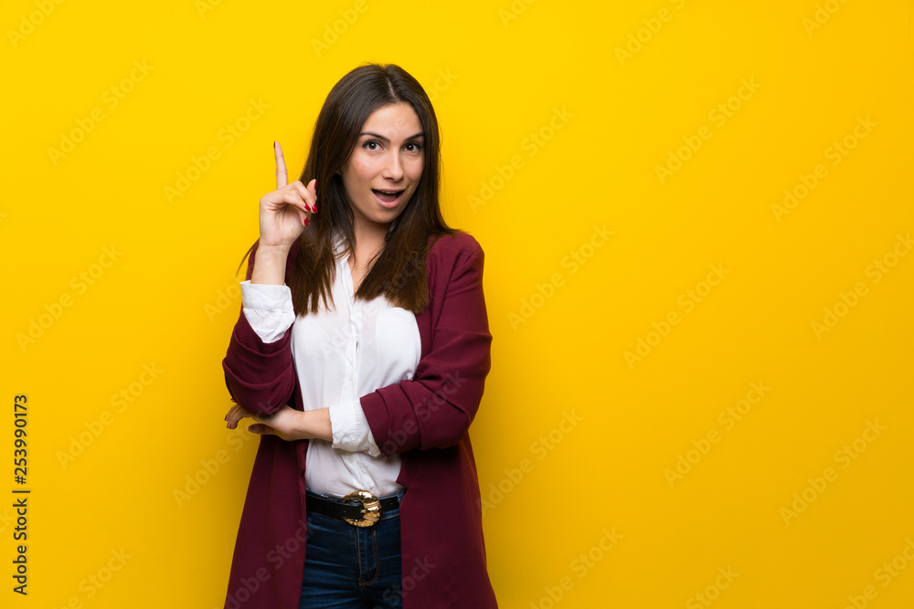 Young woman over yellow wall thinking an idea pointing the finger up Young woman over yellow wall thinking an idea pointing the finger up
