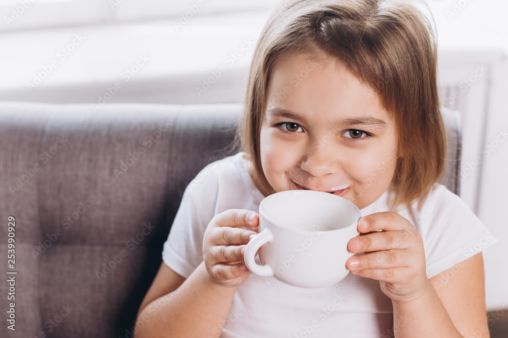 Cheerful cute adorable girl drinking milk in a cup at home Cheerful cute adorable girl drinking milk in a cup at home