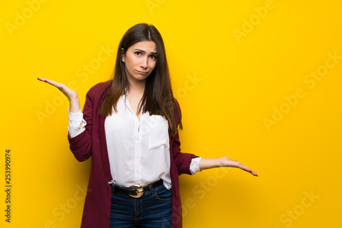Young woman over yellow wall unhappy because not understand something