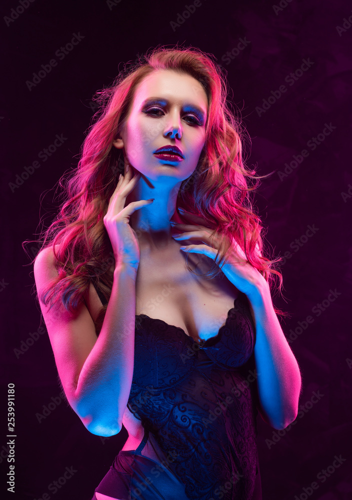 Beautiful slim sexy busty blonde girl wearing black bodysuit lit up in pink  and blue light