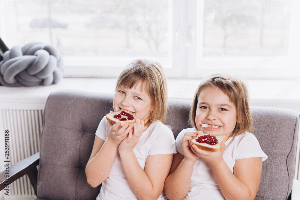 Family breakfast at home. Two girls sisters have a breakfast, eating sandwich with strawberry jam Family breakfast at home. Two girls sisters have a breakfast, eating sandwich with strawberry jam