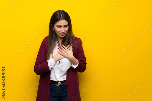 Young woman over yellow wall having a pain in the heart