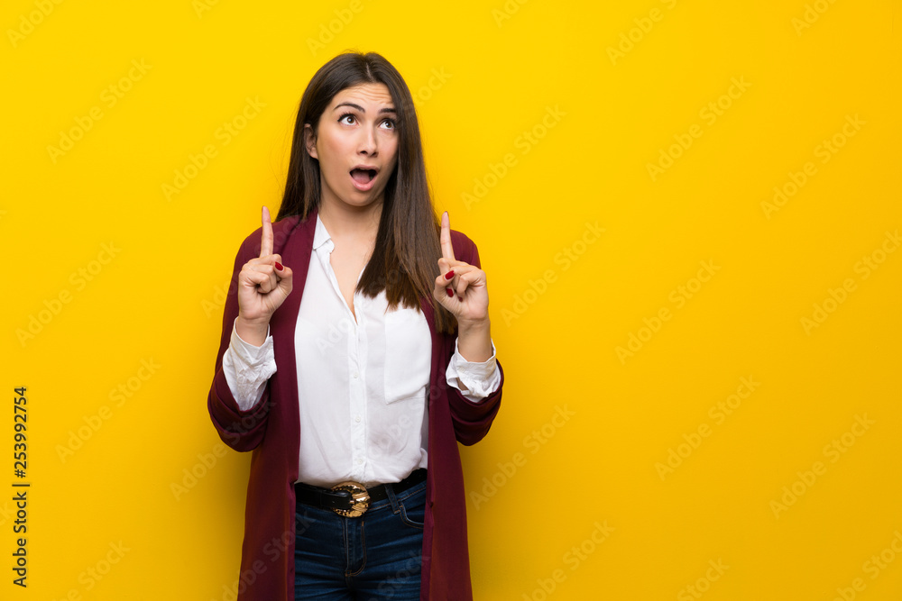 Young woman over yellow wall surprised and pointing up Young woman over yellow wall surprised and pointing up