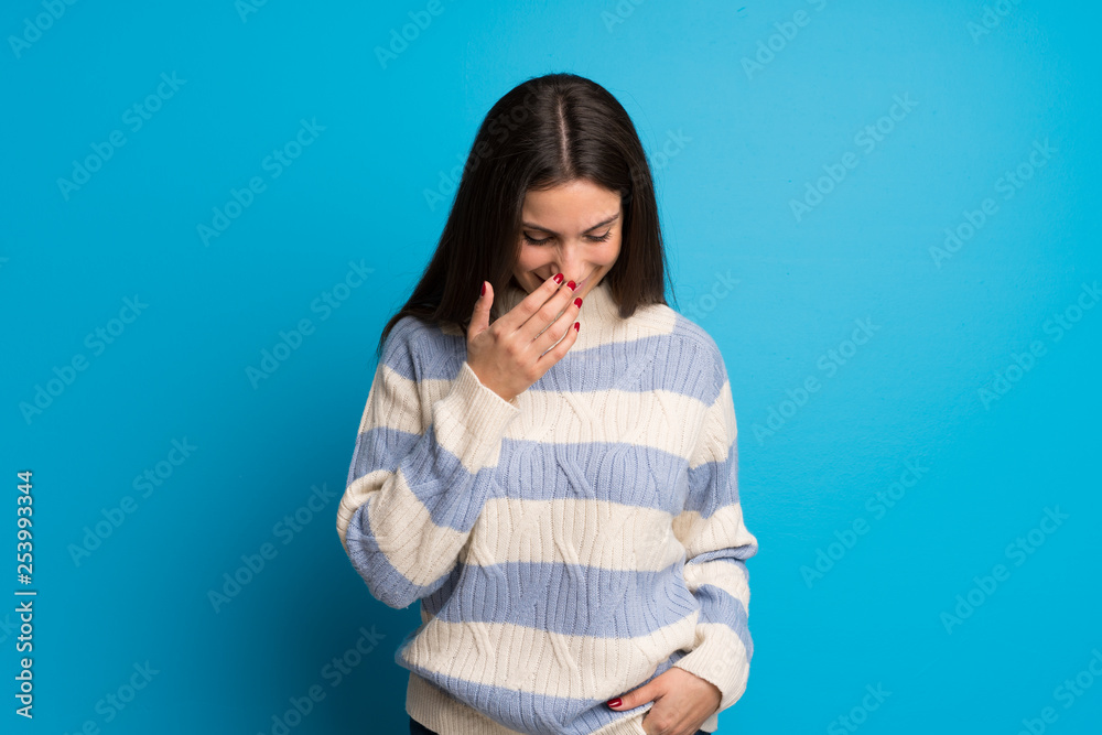 Young woman over blue wall posing with arms at hip and laughing Young woman over blue wall posing with arms at hip and laughing