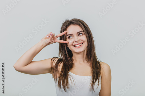 The girl salutes on a white background. The shadowy shot of a charming young woman, showing the v sign over his forehead, looks aside and smiles grimly, trying to strike or seduce someone.