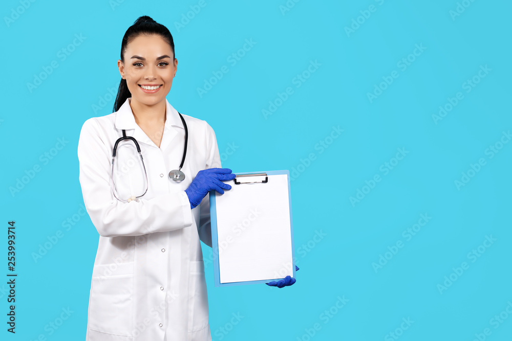 Attractive young woman doctor with stethoscope holding clipboard over blue background. Attractive young woman doctor with stethoscope holding clipboard over blue background.