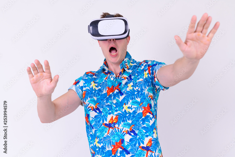 Portrait of young shocked tourist man using virtual reality headset with arms raised Portrait of young shocked tourist man using virtual reality headset with arms raised