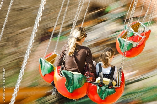 Mother with daughter moving fast on carousel. Motion blur captured, focused on bodies.