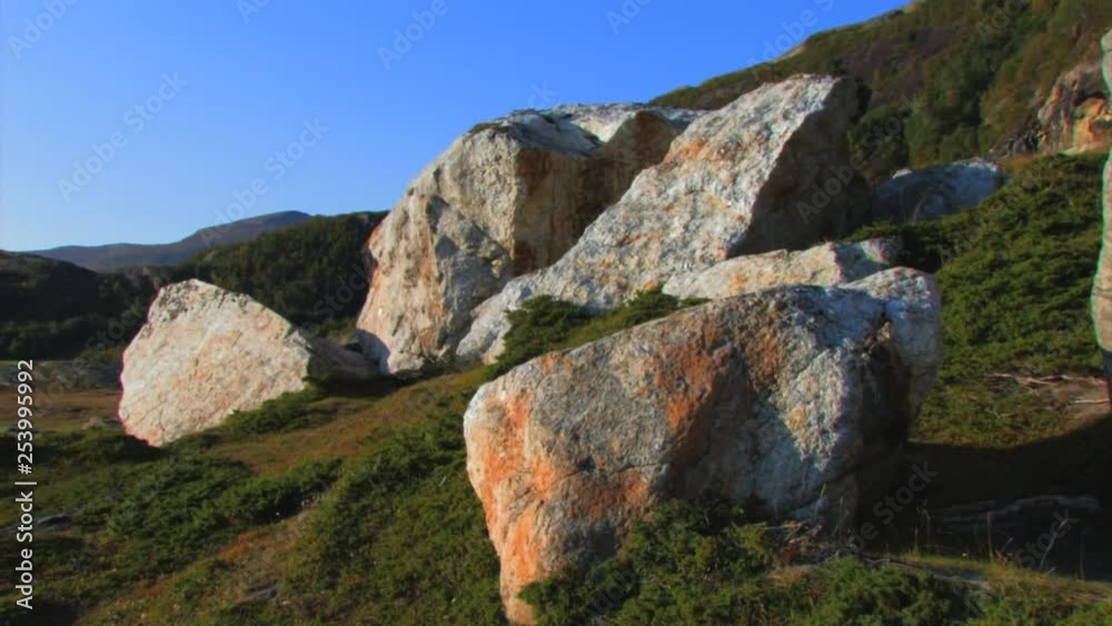 Boulders on a grassy hillside. Rolling hills and a bright blue sky on the horizon in the arctic. PAN RIGHT. Boulders on a grassy hillside. Rolling hills and a bright blue sky on the horizon in the arctic. PAN RIGHT.