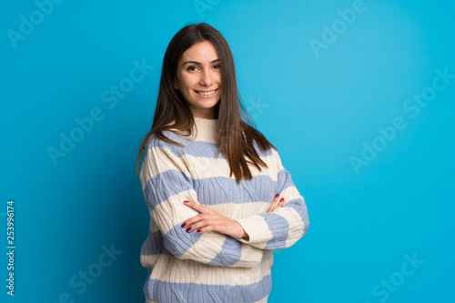 Young woman over blue wall with arms crossed