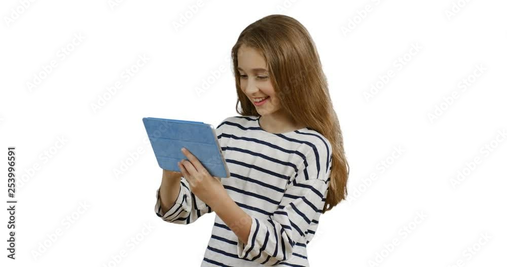 Pretty teen girl with long hair standing on the white wall background and scrolling or tapping on the tablet computer screen. Pretty teen girl with long hair standing on the white wall background and scrolling or tapping on the tablet computer screen.