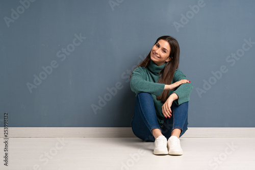 Young woman sitting on the floor posing with arms at hip and smiling
