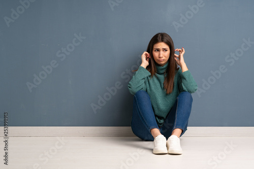 Young woman sitting on the floor frustrated and covering ears with hands