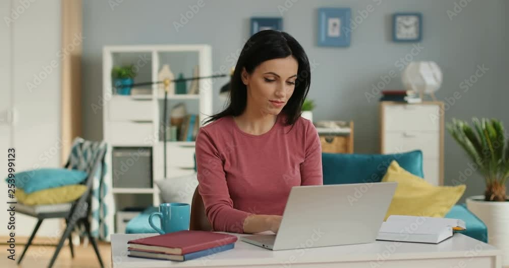 Caucasian beautiful young brunette woman in pink blouse working at the laptop computer as freelancer at home. Caucasian beautiful young brunette woman in pink blouse working at the laptop computer as freelancer at home.