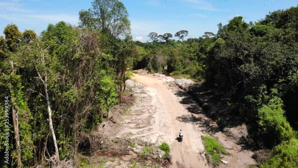 Single Motorbike Rider Driving Along Jungle Dirt Road, Cambodia. Single Motorbike Rider Driving Along Jungle Dirt Road, Cambodia.