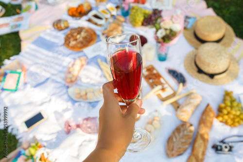 Woman hold wineglass with red champagne at picnic layout background