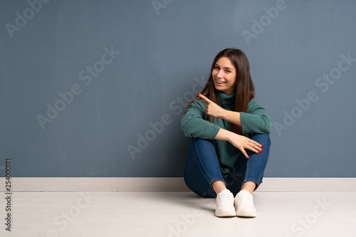 Young woman sitting on the floor pointing to the side to present a product