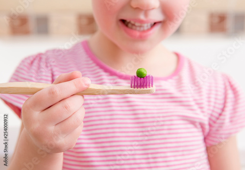 Obraz na plátne Selective focus on bamboo tooth brush with green pea on it and smiling blurred anonymous girl on background