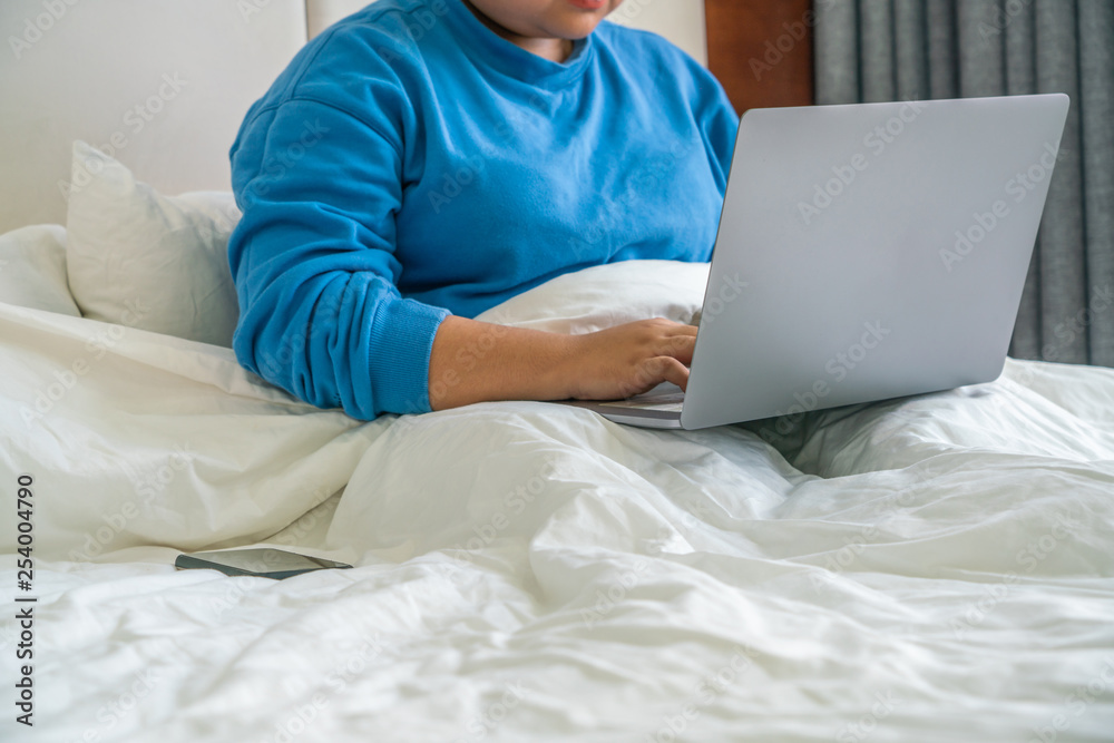 Young woman sitting on bed and working on laptop Young woman sitting on bed and working on laptop