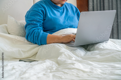 Young woman sitting on bed and working on laptop
