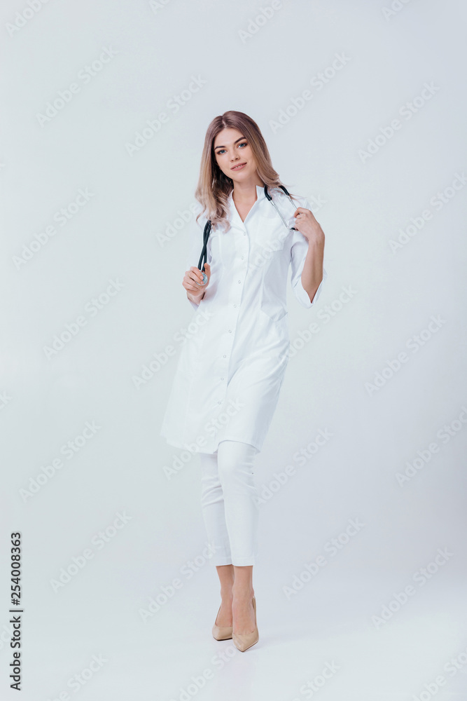 Full length portrait of medical physician doctor woman in white coat with stethoscope looks at camera on light background. Full length portrait of medical physician doctor woman in white coat with stethoscope looks at camera on light background.