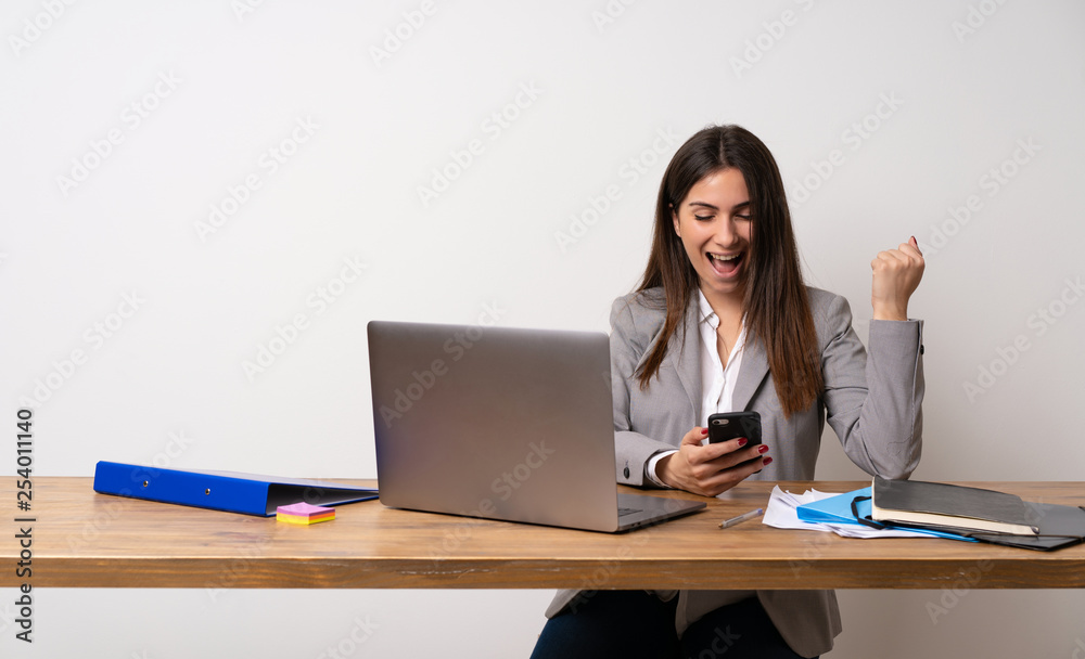 Business woman in a office with phone in victory position Business woman in a office with phone in victory position