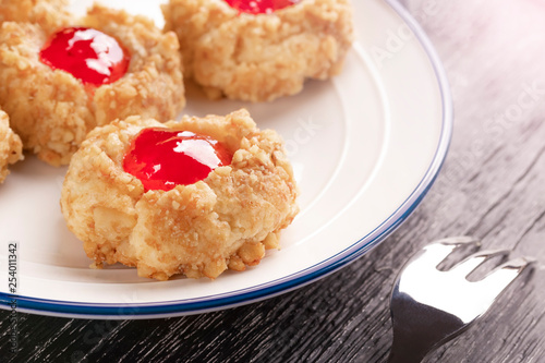 Cookies made from hazelnut shortcake with strawberry jam inside on a white plate with a patterned dessert fork.