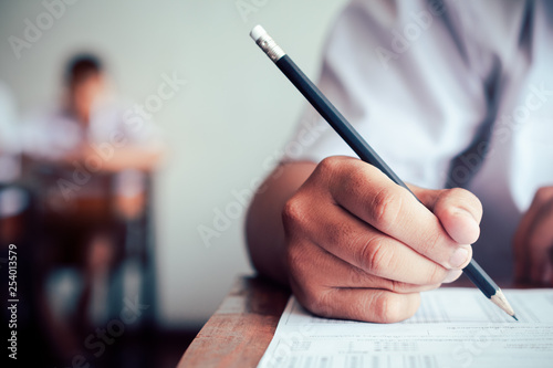Hand of student is taking exam and writing answer in classroom for education test concept