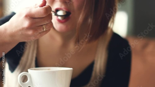 young happy woman drinks coffee, stirring with a spoon milk foam