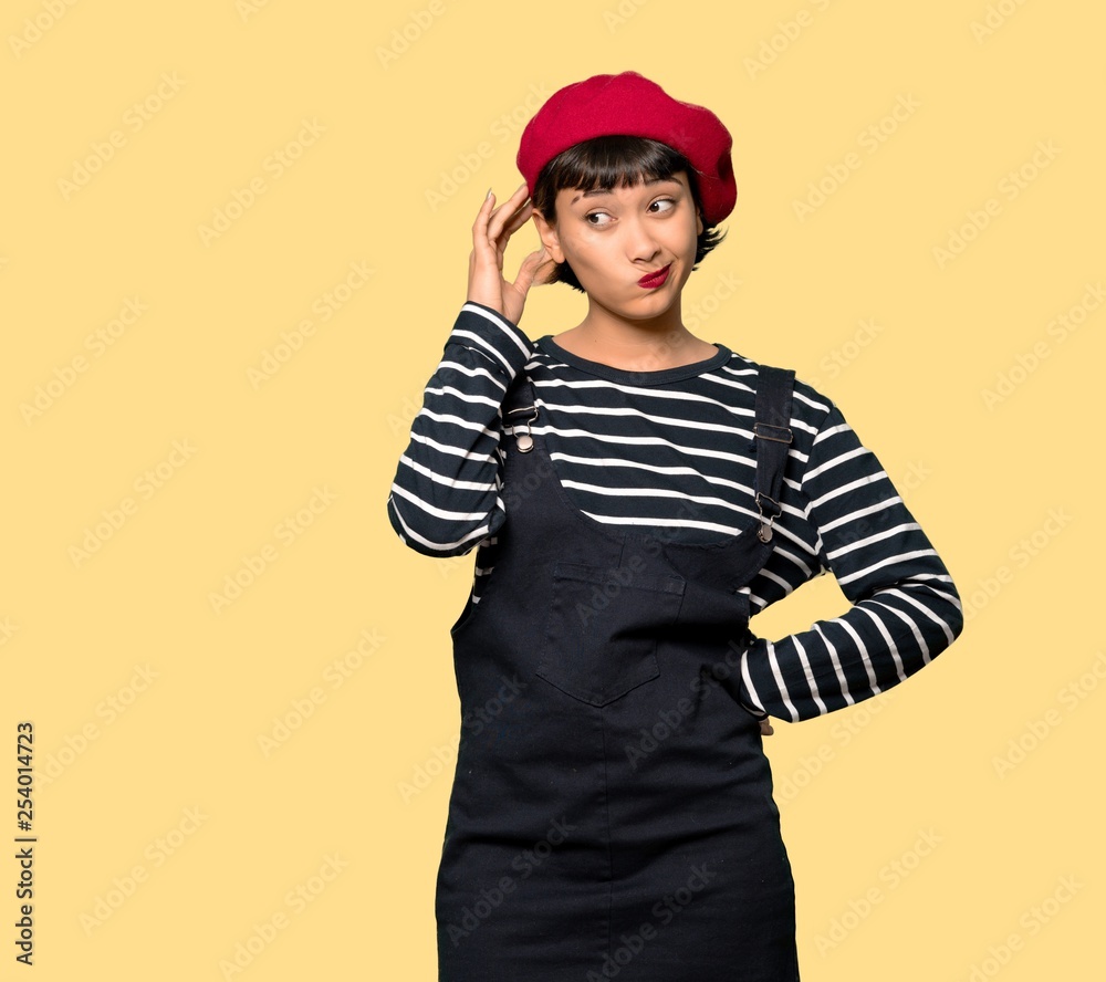 Young woman with beret with an expression of frustration and not understanding over yellow background Young woman with beret with an expression of frustration and not understanding over yellow background