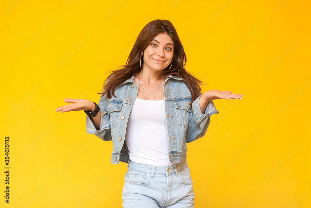I don't know. Portrait of confused beautiful brunette young woman with makeup in denim casual style standing with raised arms and looking at camera. indoor studio shot, isolated on yellow background. I don't know. Portrait of confused beautiful brunette young woman with makeup in denim casual style standing with raised arms and looking at camera. indoor studio shot, isolated on yellow background.