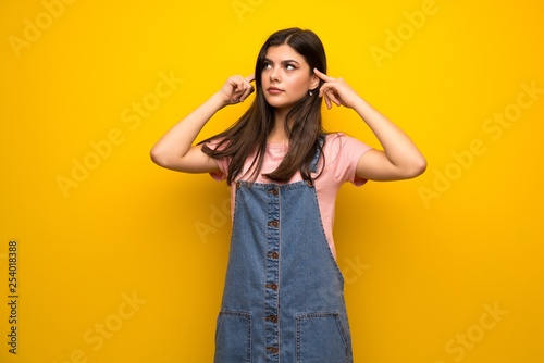 Teenager girl over yellow wall having doubts and thinking