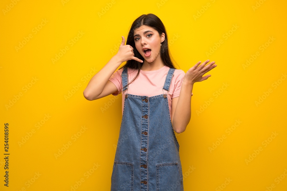 Teenager girl over yellow wall making phone gesture and doubting Teenager girl over yellow wall making phone gesture and doubting