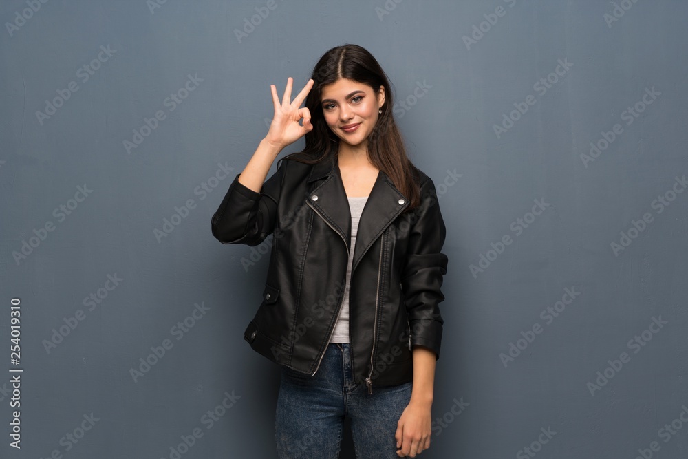 Teenager girl over grey wall showing ok sign with fingers Teenager girl over grey wall showing ok sign with fingers