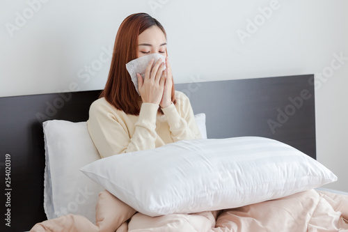 Young woman wear yellow sweater got nose allergy, flu sneezing nose sitting in bed at home