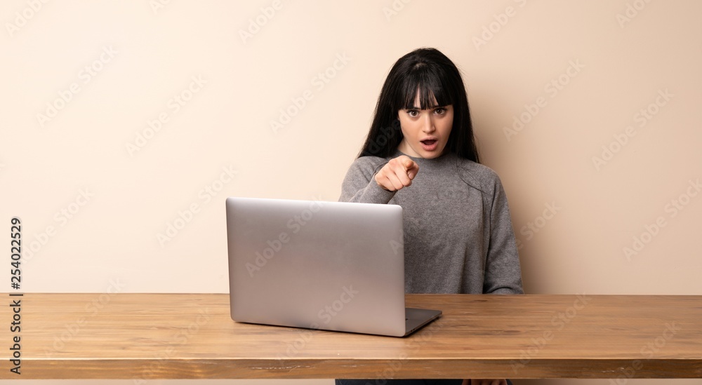Young woman working with her laptop surprised and pointing front Young woman working with her laptop surprised and pointing front