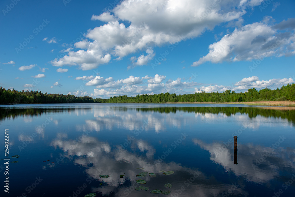 blue sky and cloud reflections in countryside lake in summer with boat and wooden boardwalk blue sky and cloud reflections in countryside lake in summer with boat and wooden boardwalk