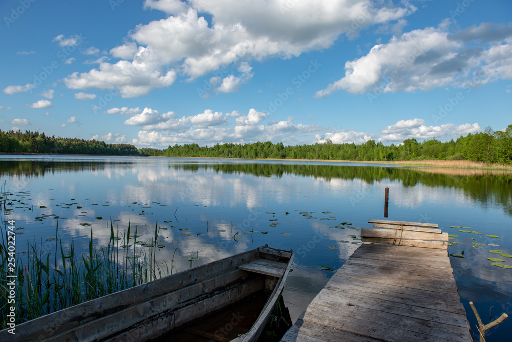 blue sky and cloud reflections in countryside lake in summer with boat and wooden boardwalk blue sky and cloud reflections in countryside lake in summer with boat and wooden boardwalk