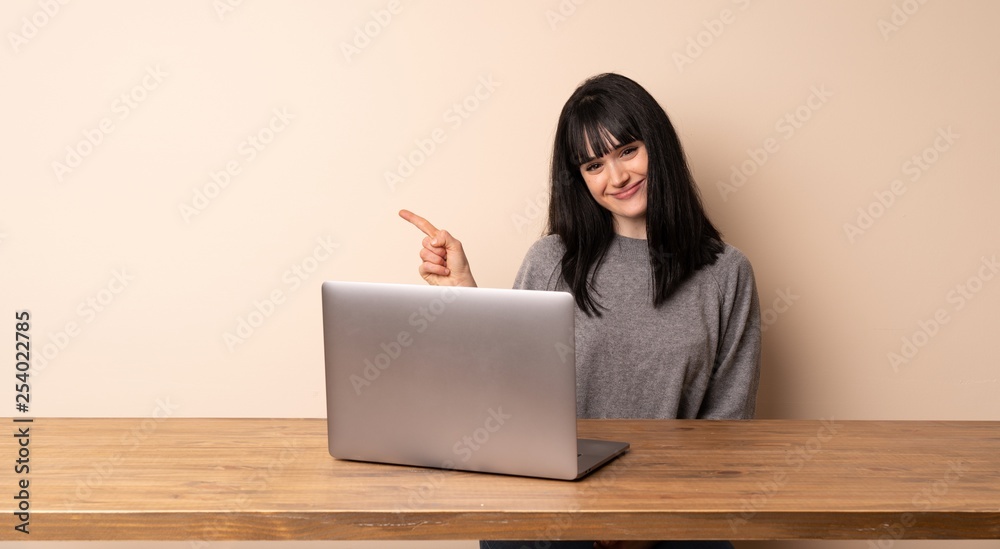 Young woman working with her laptop pointing to the side to present a product Young woman working with her laptop pointing to the side to present a product