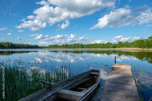 Fototapeta Naklejka Na Ścianę i Meble -  blue sky and cloud reflections in countryside lake in summer with boat and wooden boardwalk