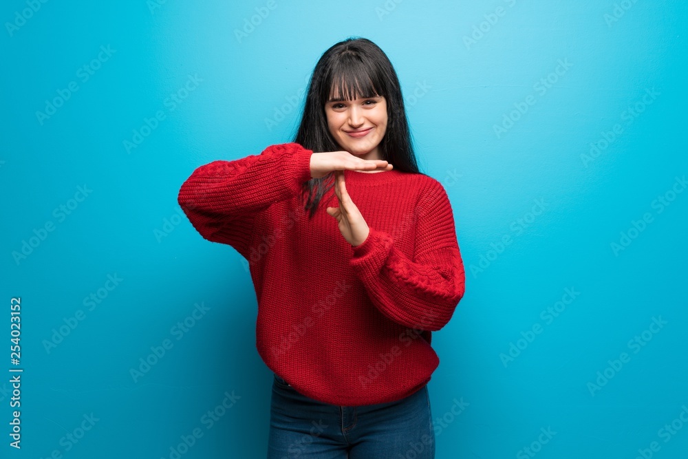 Woman with red sweater over blue wall making time out gesture Woman with red sweater over blue wall making time out gesture