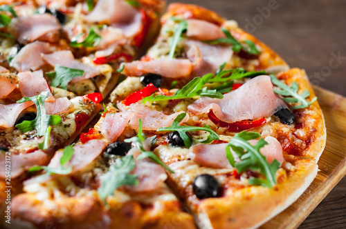 Pizza with Mozzarella cheese, ham, pepper, olive, meat, Tomato sauce, Spices and Fresh arugula. Italian pizza on wooden background