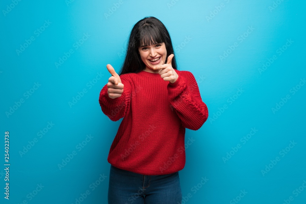 Woman with red sweater over blue wall pointing to the front and smiling Woman with red sweater over blue wall pointing to the front and smiling
