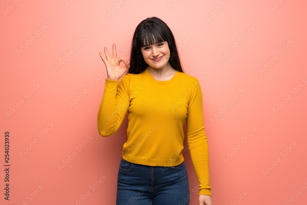 Woman with yellow sweater over pink wall showing ok sign with fingers Woman with yellow sweater over pink wall showing ok sign with fingers