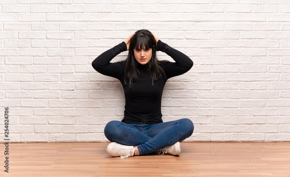 Woman sitting on the floor frustrated and takes hands on head Woman sitting on the floor frustrated and takes hands on head