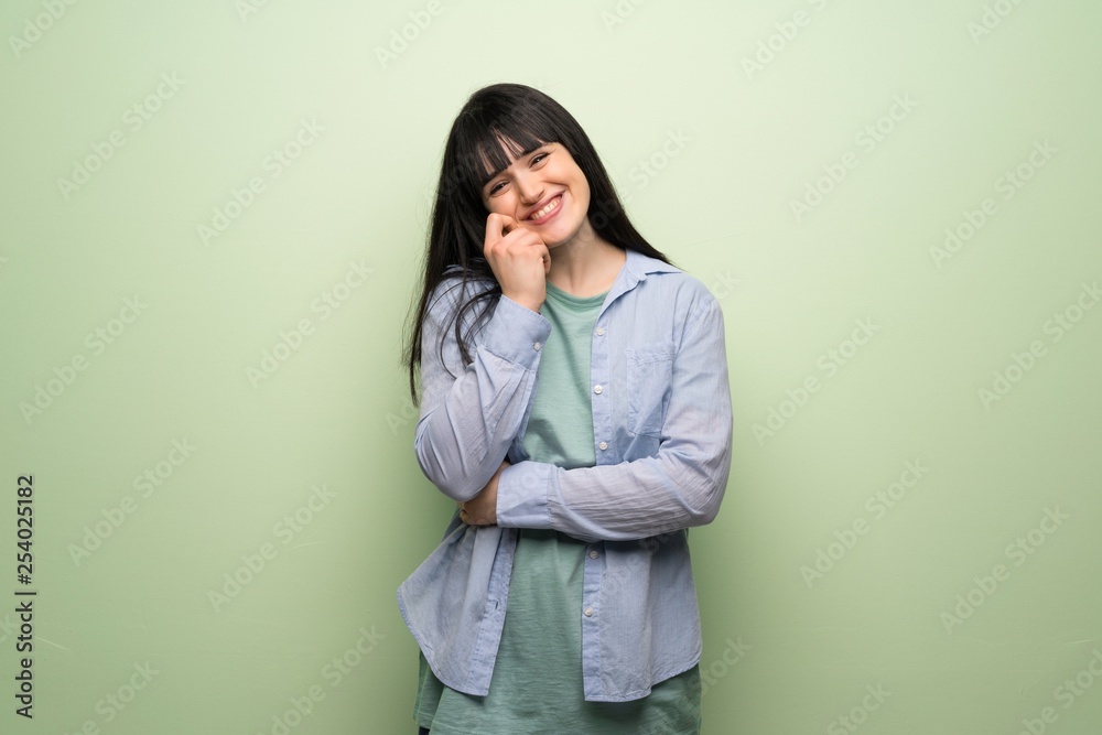 Young woman over green wall smiling with a sweet expression Young woman over green wall smiling with a sweet expression