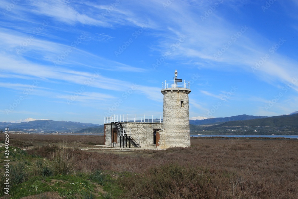 Old stone lighthouse tower and beacon at the Ambracian (Amvrakikos) gulf wetland at Kopraina village in Arta region in Epirus Greece at winter with white clouds and blue sky in a sunny day
