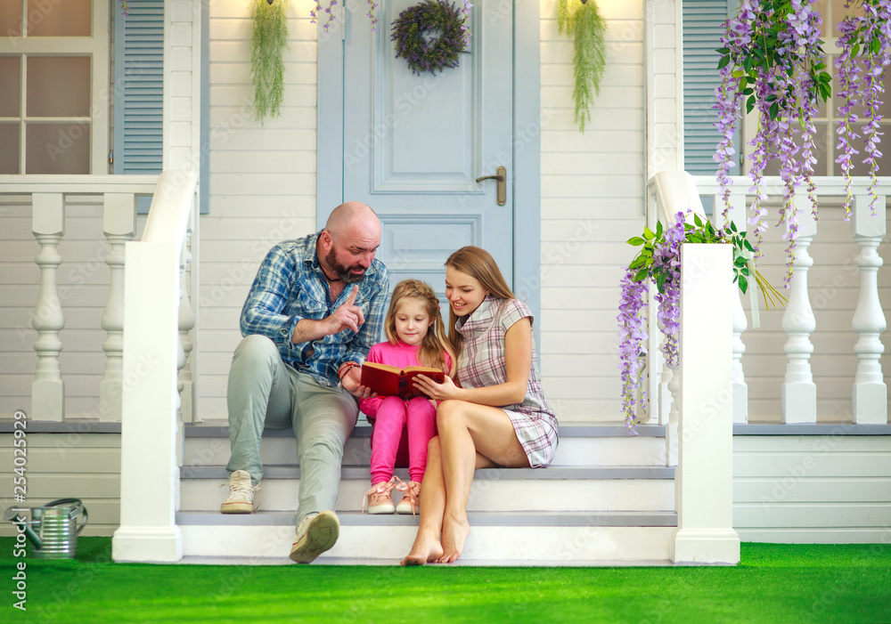 Φωτογραφία Parents mother and father read a book with their daughter in the courtyard of a